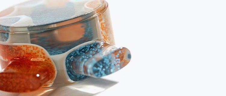 Close-up view of a 3D-printed, clear part with orange and blue particles scattered throughout on its side